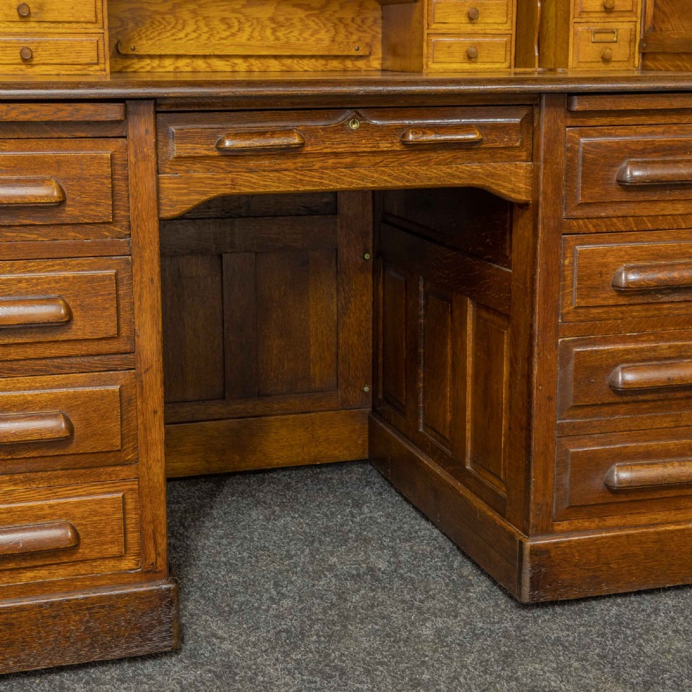 An Edwardian oak roll top desk featuring an S-curve slatted shutter opening to a fitted interior with small drawers and pigeonholes above twin pedestal drawers. View VIII