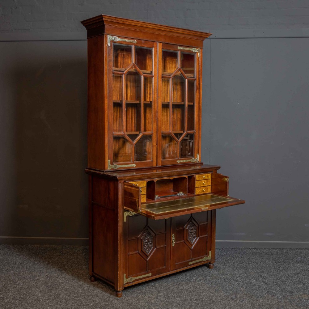 A tall Victorian walnut secretaire bookcase featuring a glazed upper display section, a drop-down desk compartment, and carved double doors at the base with decorative brass mounts.
