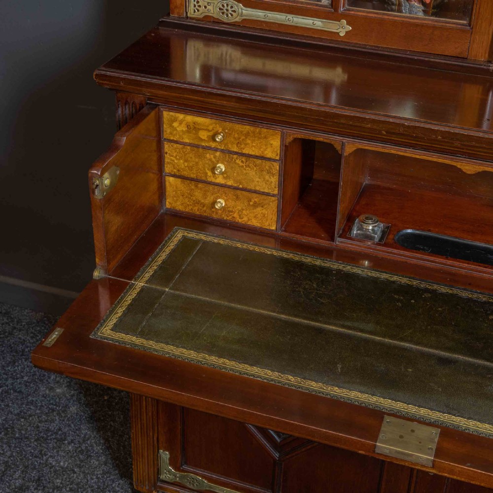 A tall Victorian walnut secretaire bookcase featuring a glazed upper display section, a drop-down desk compartment, and carved double doors at the base with decorative brass mounts. View VI