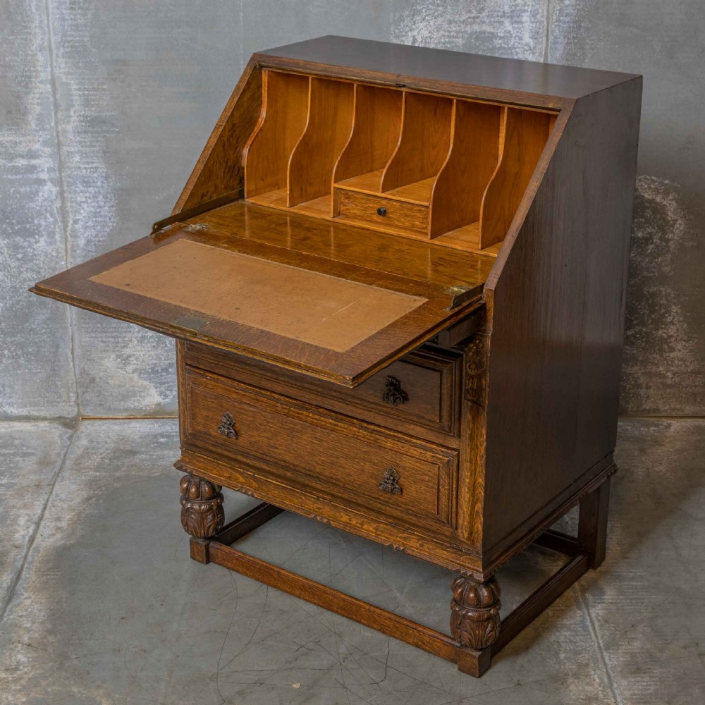An early 20th-century dark oak writing bureau with a carved oval floral motif on the sloped flap above two drawers. View II