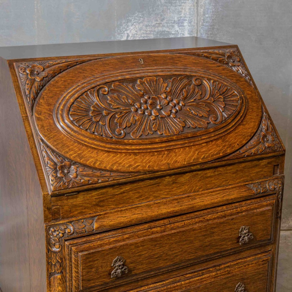 An early 20th-century dark oak writing bureau with a carved oval floral motif on the sloped flap above two drawers. View IV