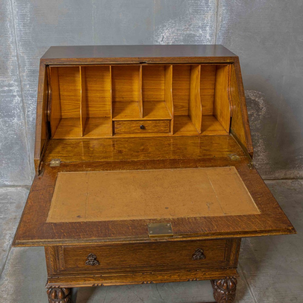 An early 20th-century dark oak writing bureau with a carved oval floral motif on the sloped flap above two drawers. View V