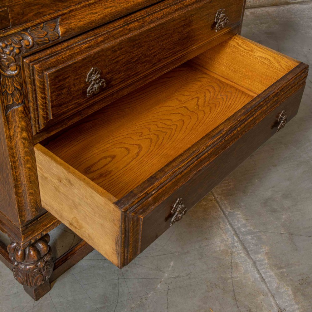 An early 20th-century dark oak writing bureau with a carved oval floral motif on the sloped flap above two drawers. View VI