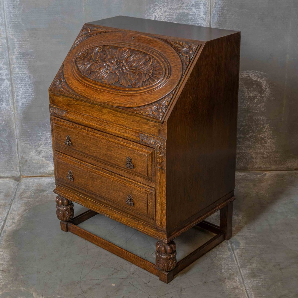 An early 20th-century dark oak writing bureau with a carved oval floral motif on the sloped flap above two drawers. View VIII
