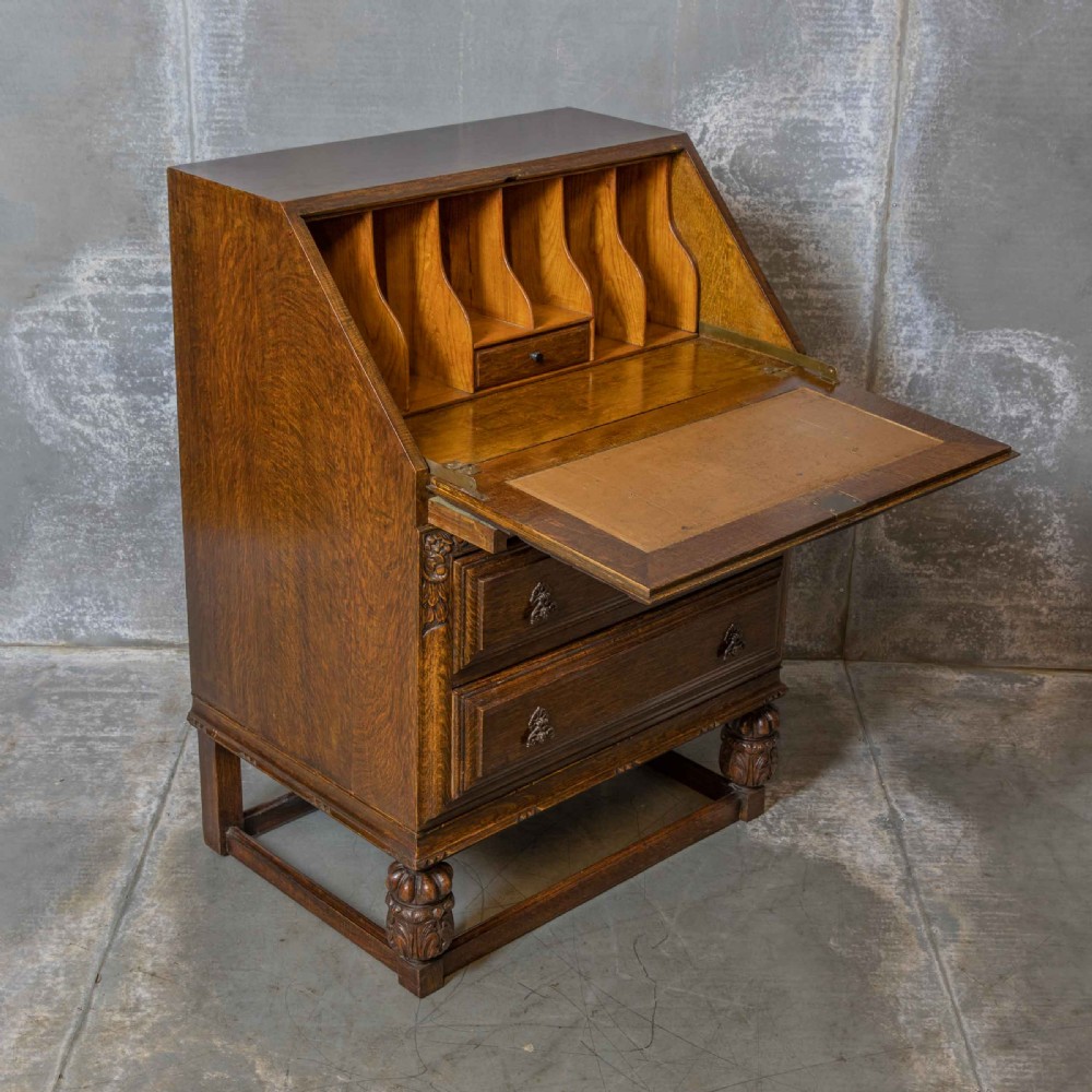 An early 20th-century dark oak writing bureau with a carved oval floral motif on the sloped flap above two drawers. View X
