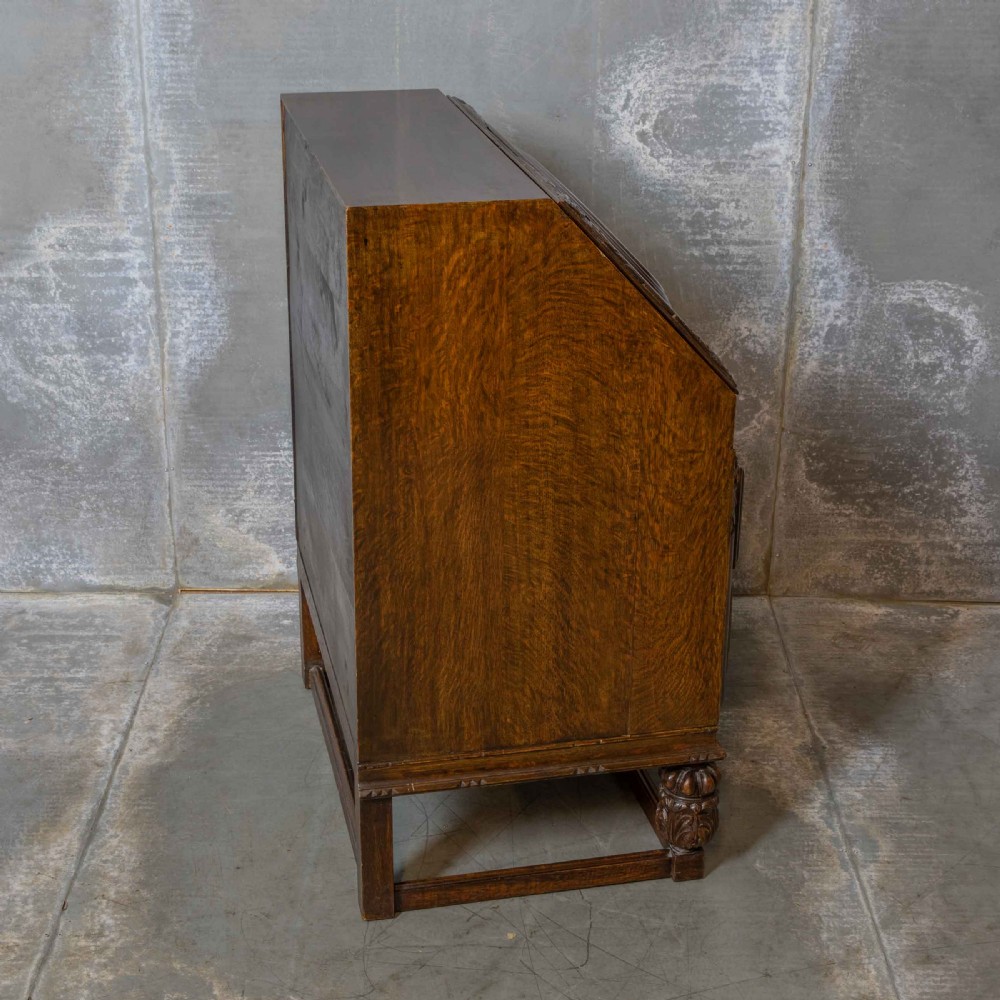An early 20th-century dark oak writing bureau with a carved oval floral motif on the sloped flap above two drawers. View XI