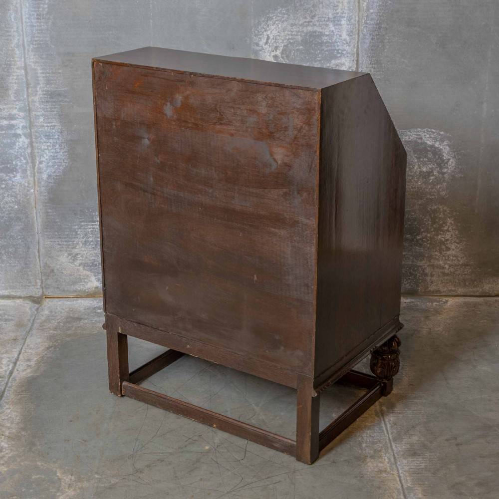 An early 20th-century dark oak writing bureau with a carved oval floral motif on the sloped flap above two drawers. View XII