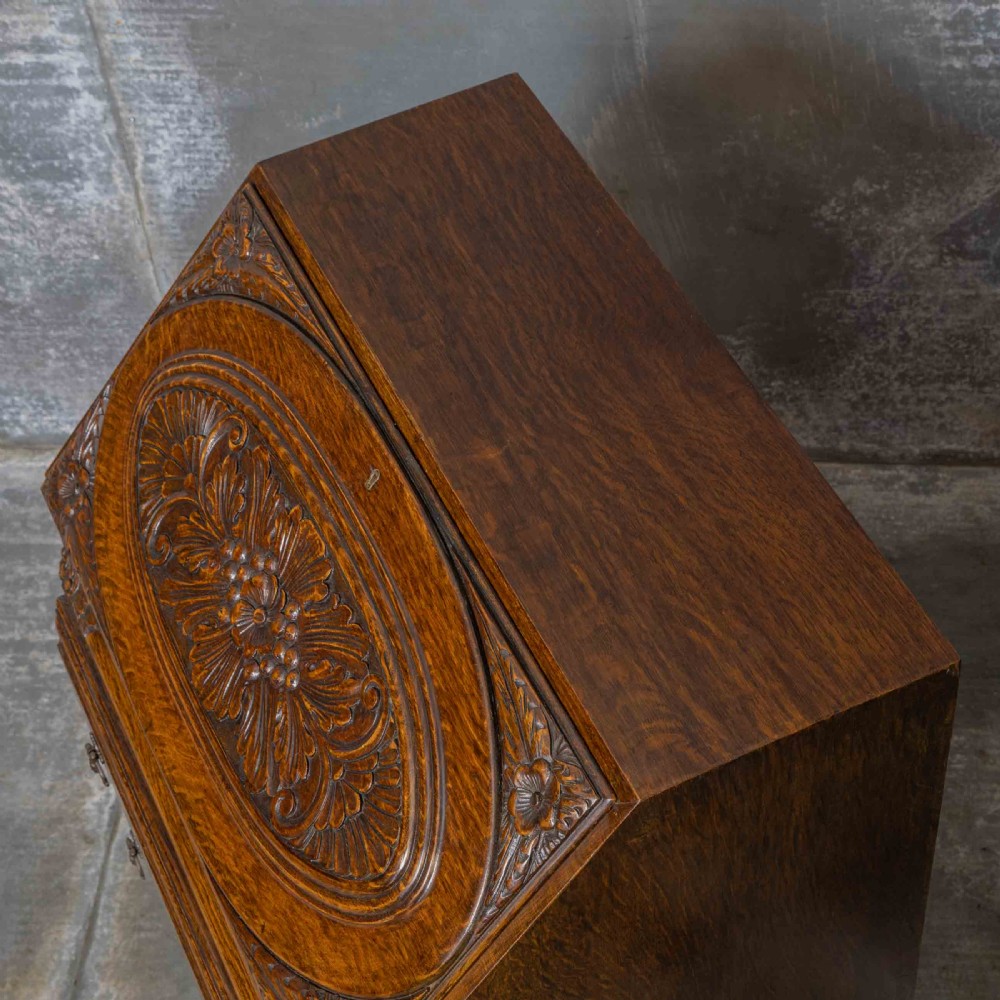 An early 20th-century dark oak writing bureau with a carved oval floral motif on the sloped flap above two drawers. View XIII