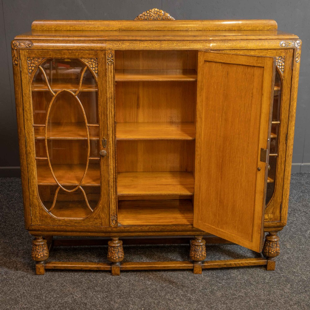 An early 20th-century carved oak display cabinet with a central carved floral panel door flanked by two oval-pattern glazed doors set on turned legs with stretchers. View V
