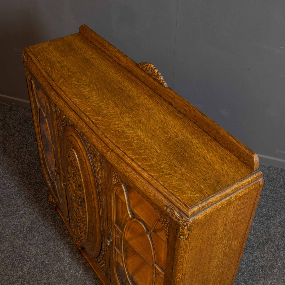 An early 20th-century carved oak display cabinet with a central carved floral panel door flanked by two oval-pattern glazed doors set on turned legs with stretchers. View X