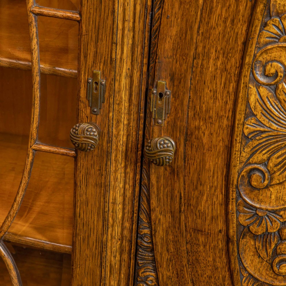An early 20th-century carved oak display cabinet with a central carved floral panel door flanked by two oval-pattern glazed doors set on turned legs with stretchers. View XIII