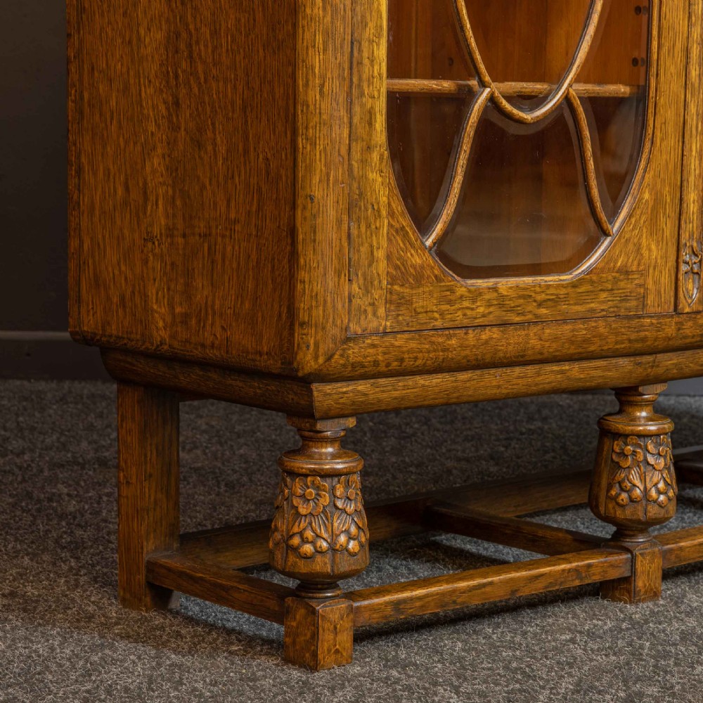 An early 20th-century carved oak display cabinet with a central carved floral panel door flanked by two oval-pattern glazed doors set on turned legs with stretchers. View XIV