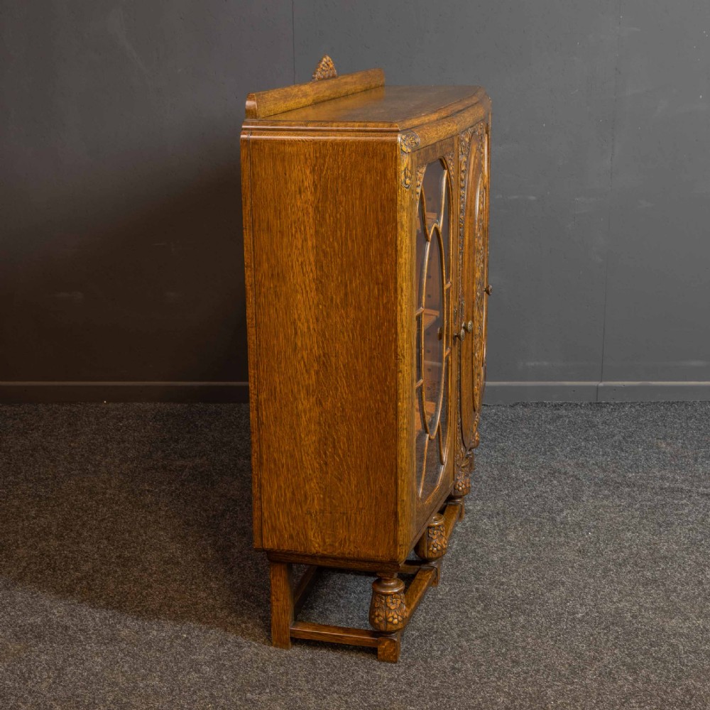 An early 20th-century carved oak display cabinet with a central carved floral panel door flanked by two oval-pattern glazed doors set on turned legs with stretchers. View XV