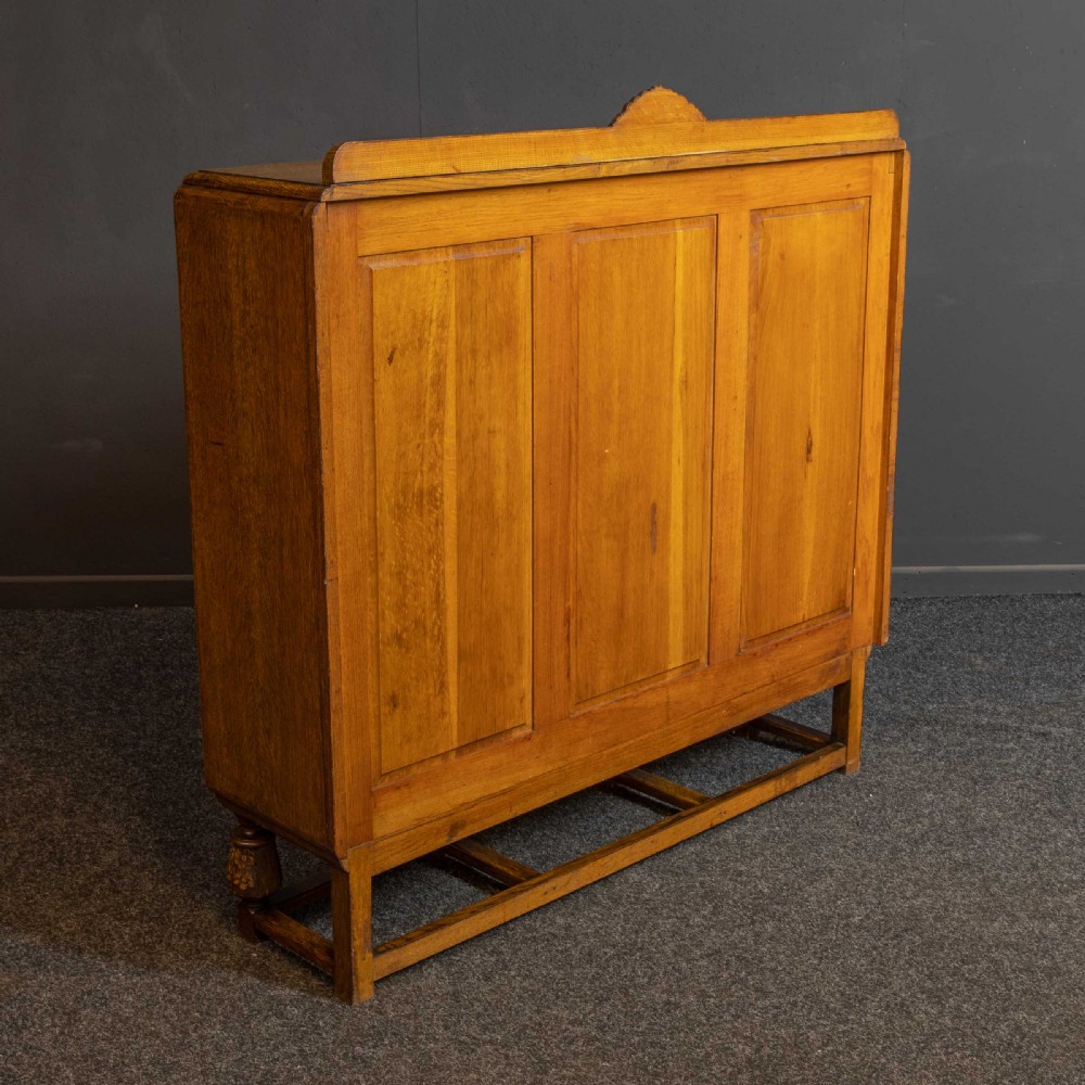 An early 20th-century carved oak display cabinet with a central carved floral panel door flanked by two oval-pattern glazed doors set on turned legs with stretchers. View XVI