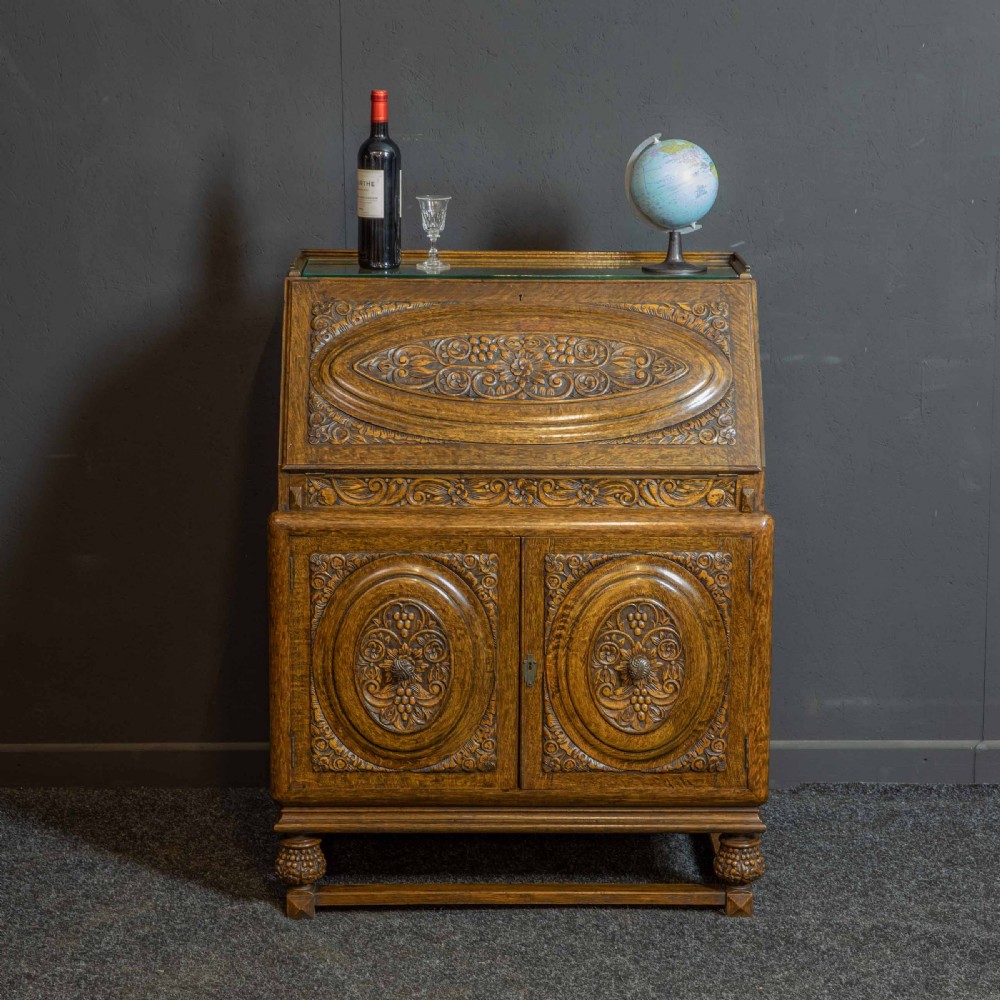 A medium brown carved oak writing bureau with a slant front lid above a double door cupboard, detailed with carved oval foliate panels and turned feet. View II