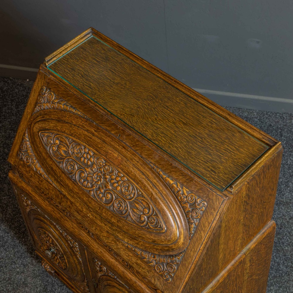 A medium brown carved oak writing bureau with a slant front lid above a double door cupboard, detailed with carved oval foliate panels and turned feet. View III