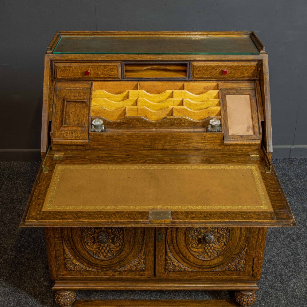 A medium brown carved oak writing bureau with a slant front lid above a double door cupboard, detailed with carved oval foliate panels and turned feet. View V