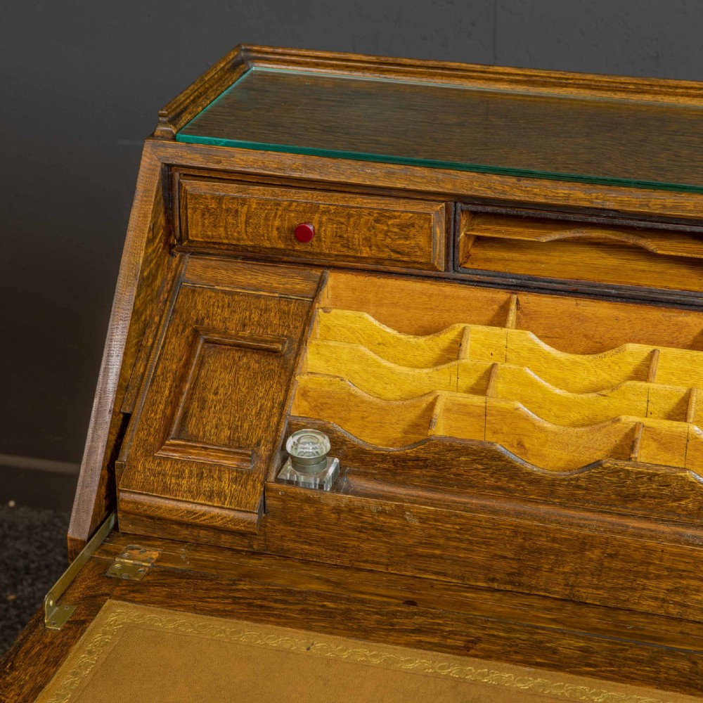 A medium brown carved oak writing bureau with a slant front lid above a double door cupboard, detailed with carved oval foliate panels and turned feet. View VII