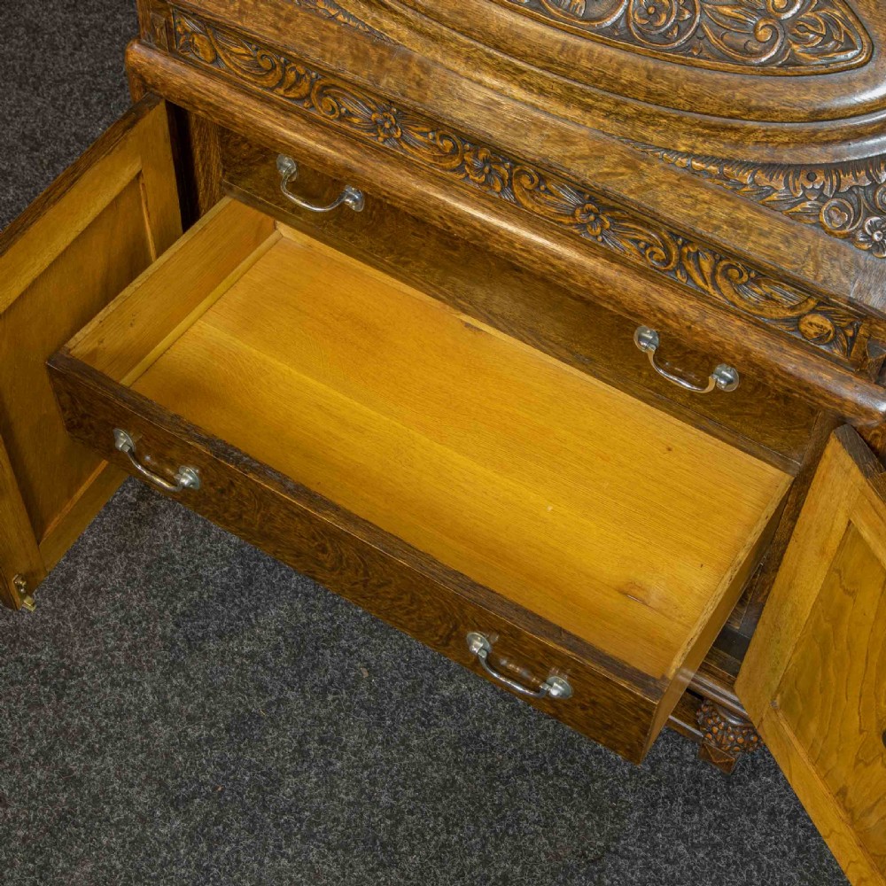 A medium brown carved oak writing bureau with a slant front lid above a double door cupboard, detailed with carved oval foliate panels and turned feet. View XI