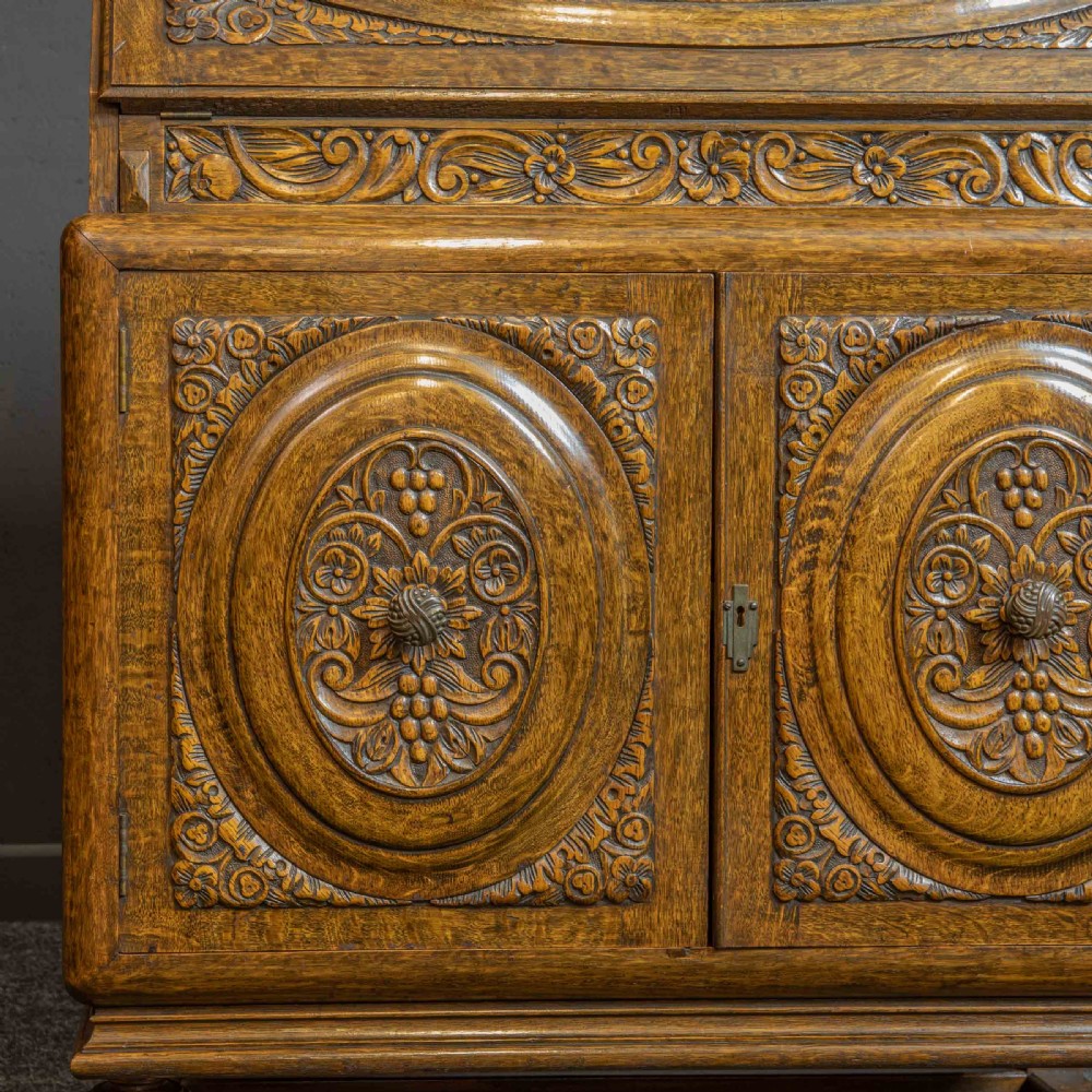 A medium brown carved oak writing bureau with a slant front lid above a double door cupboard, detailed with carved oval foliate panels and turned feet. View XII