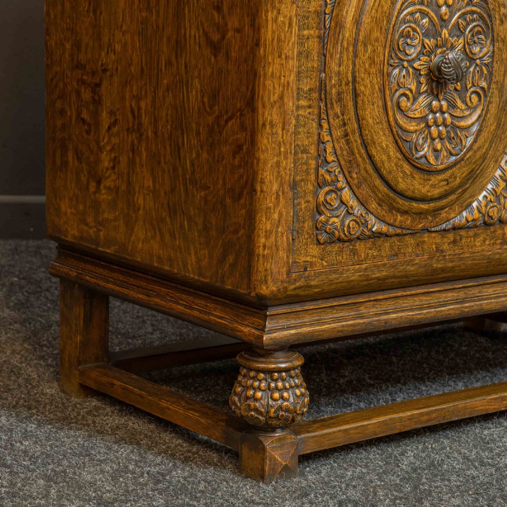 A medium brown carved oak writing bureau with a slant front lid above a double door cupboard, detailed with carved oval foliate panels and turned feet. View XIII