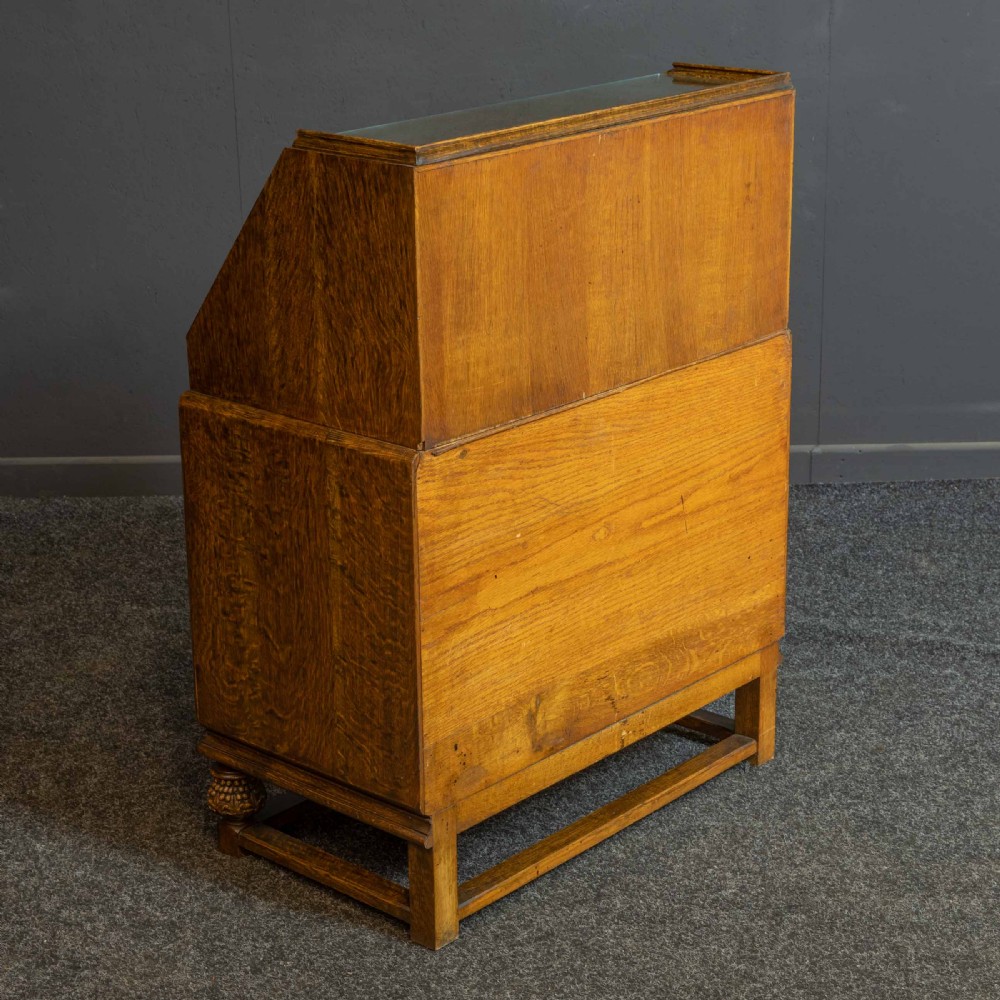 A medium brown carved oak writing bureau with a slant front lid above a double door cupboard, detailed with carved oval foliate panels and turned feet. View XVII