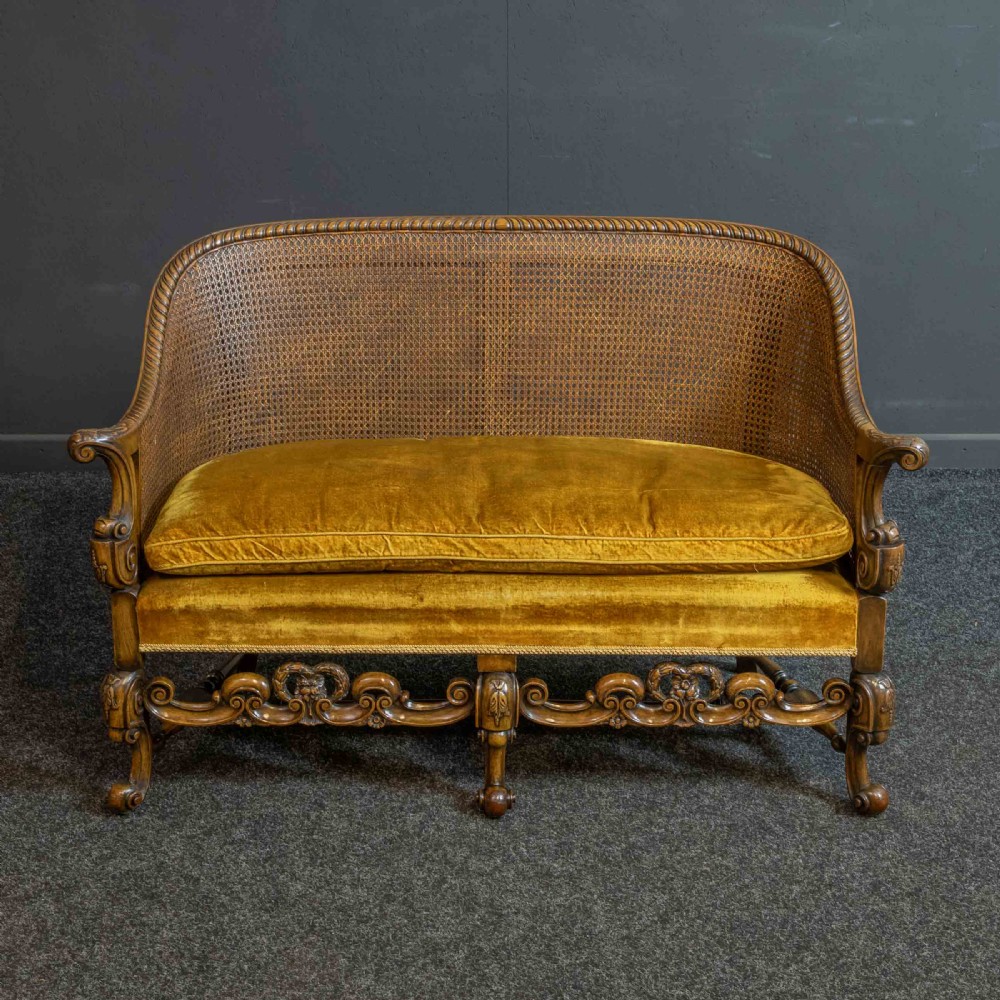 A William and Mary style walnut sofa featuring a high curved woven cane backrest, gold velvet cushion seat, and intricately carved scrollwork base. View II