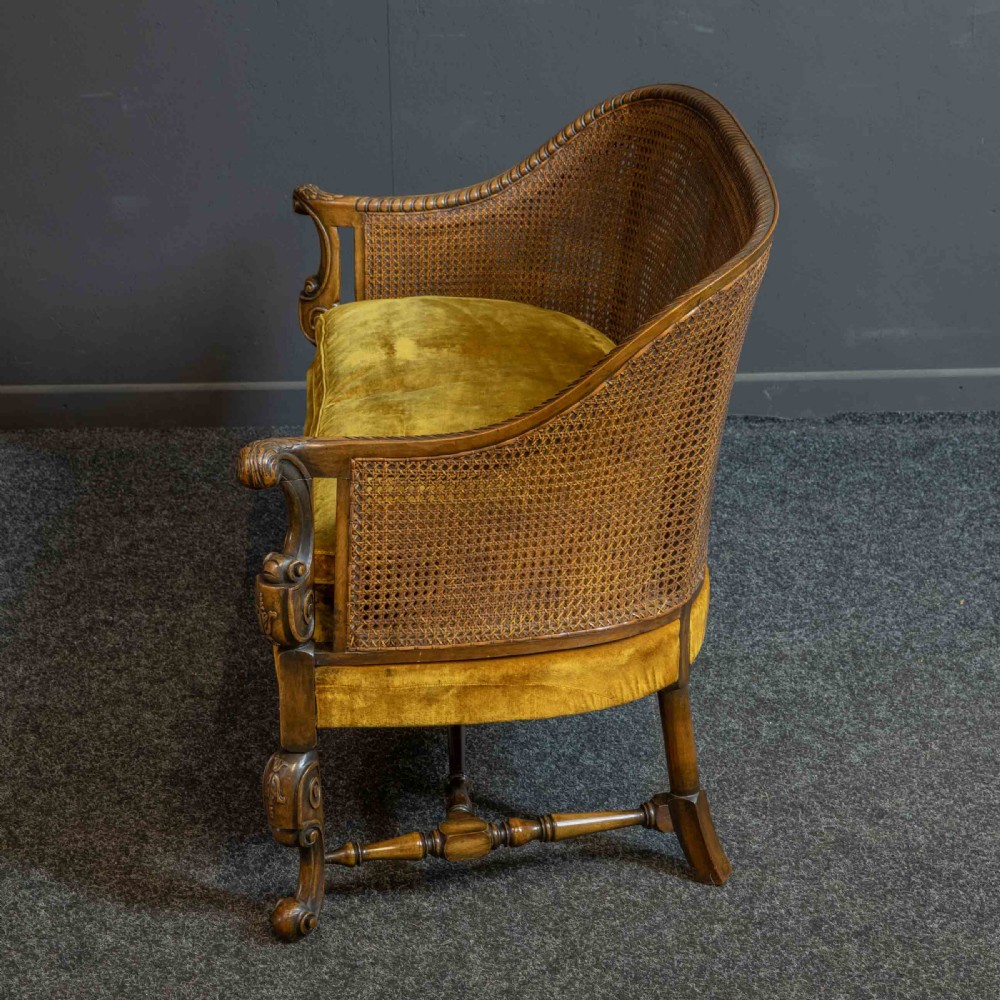 A William and Mary style walnut sofa featuring a high curved woven cane backrest, gold velvet cushion seat, and intricately carved scrollwork base. View III