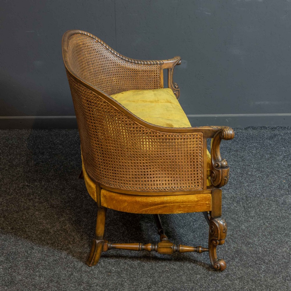 A William and Mary style walnut sofa featuring a high curved woven cane backrest, gold velvet cushion seat, and intricately carved scrollwork base. View IV