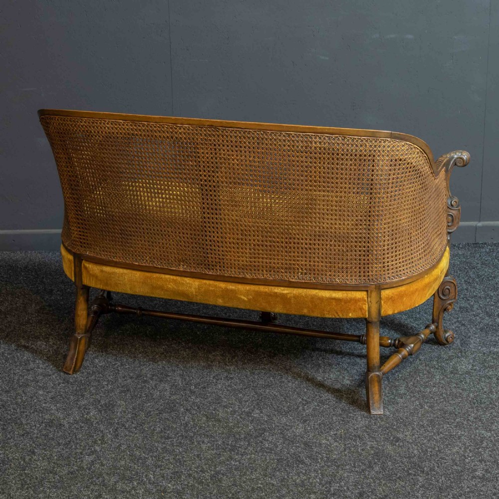 A William and Mary style walnut sofa featuring a high curved woven cane backrest, gold velvet cushion seat, and intricately carved scrollwork base. View V