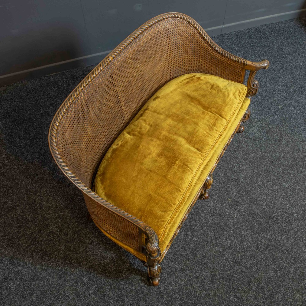 A William and Mary style walnut sofa featuring a high curved woven cane backrest, gold velvet cushion seat, and intricately carved scrollwork base. View VIII
