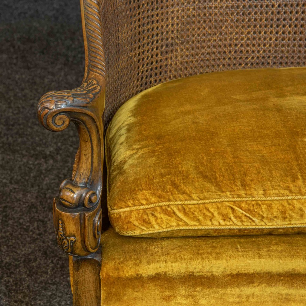 A William and Mary style walnut sofa featuring a high curved woven cane backrest, gold velvet cushion seat, and intricately carved scrollwork base. View IX