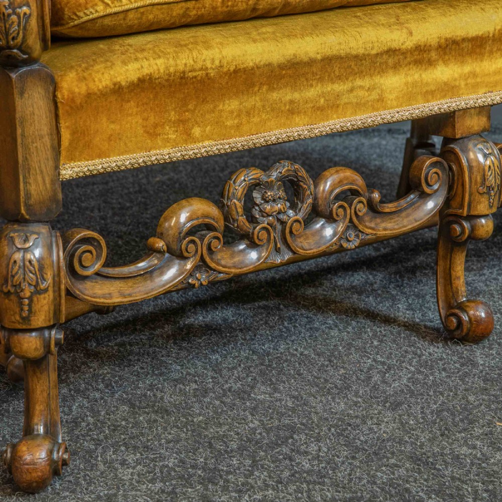 A William and Mary style walnut sofa featuring a high curved woven cane backrest, gold velvet cushion seat, and intricately carved scrollwork base. View X