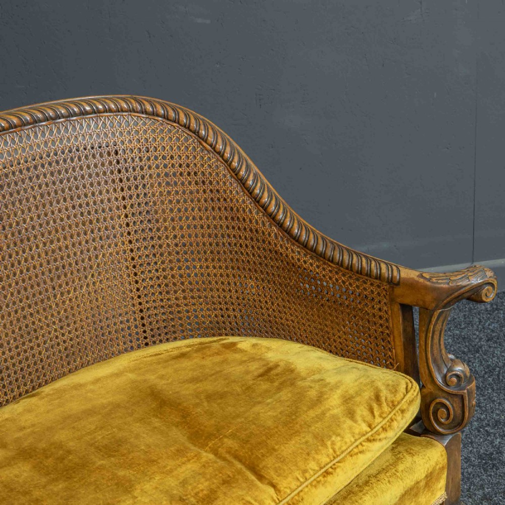 A William and Mary style walnut sofa featuring a high curved woven cane backrest, gold velvet cushion seat, and intricately carved scrollwork base. View XIII