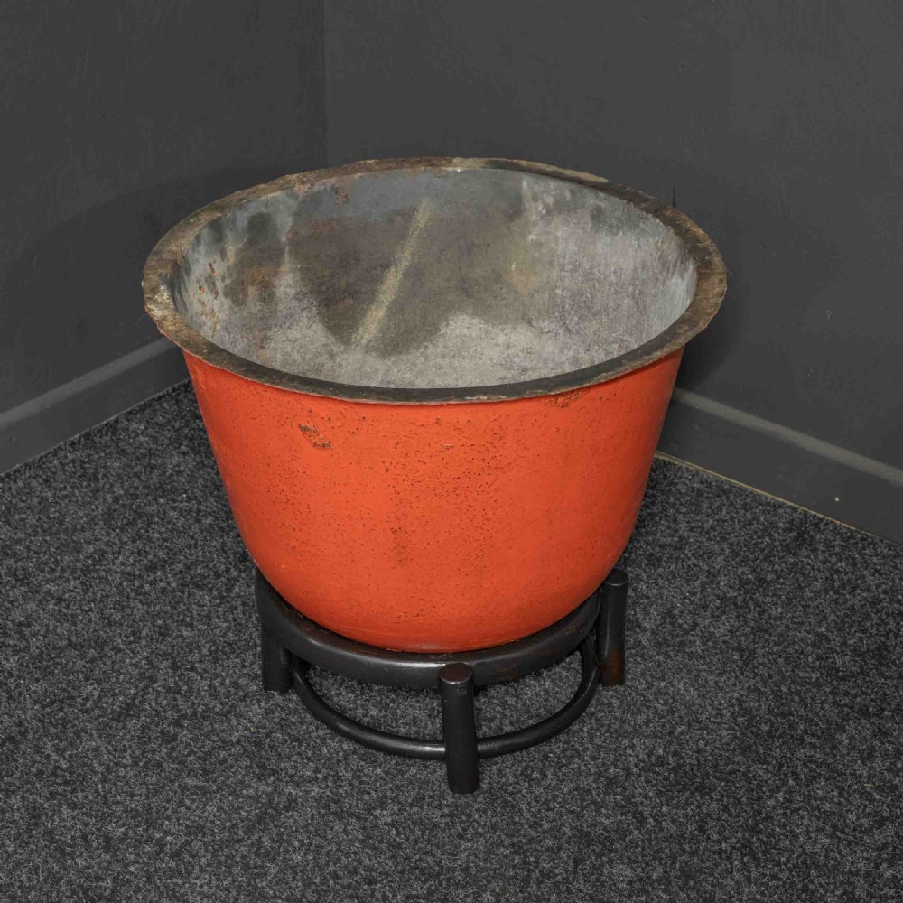A deep circular copper tub painted orange on the outer side, resting in a black circular stand.