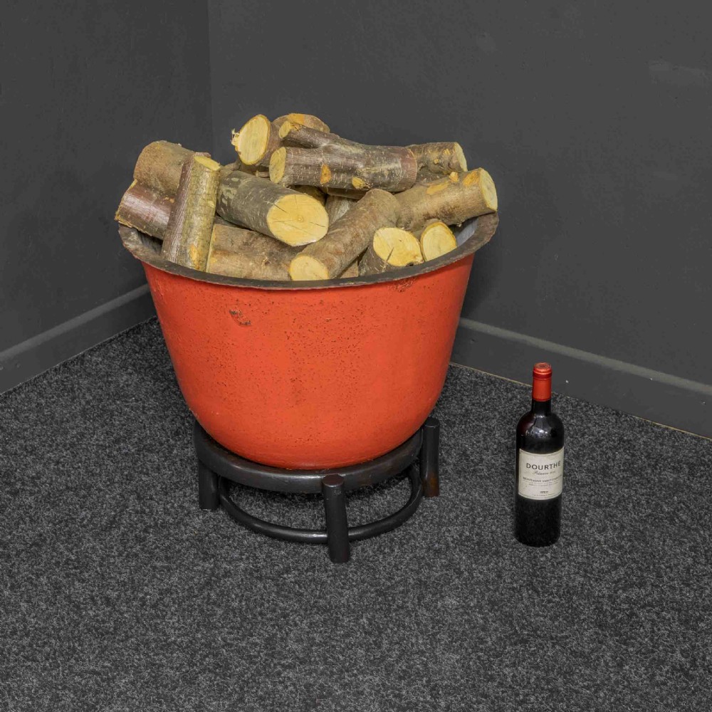 A deep circular copper tub painted orange on the outer side, resting in a black circular stand. View II
