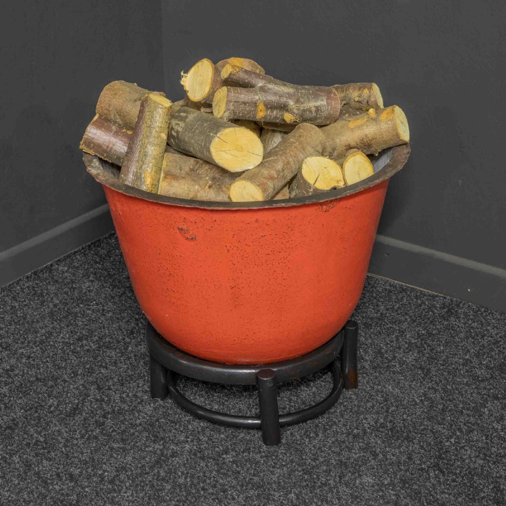 A deep circular copper tub painted orange on the outer side, resting in a black circular stand. View III
