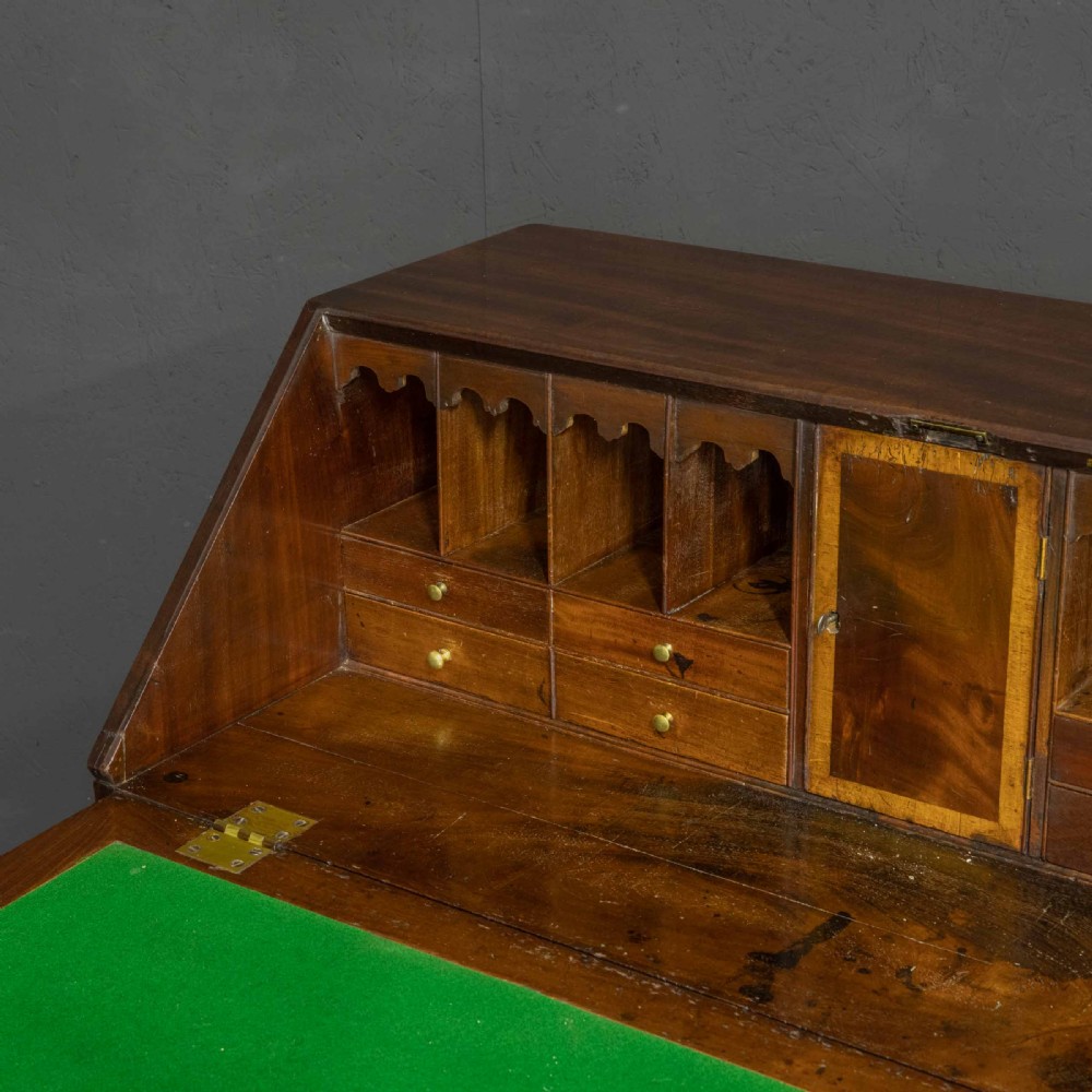 A Georgian mahogany writing bureau featuring a sloped fall-front lid above four graduated drawers with brass swan-neck handles, supported on bracket feet. View V