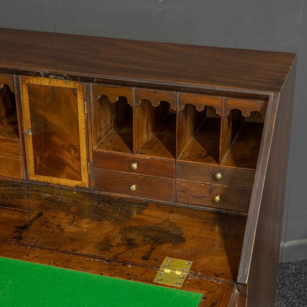 A Georgian mahogany writing bureau featuring a sloped fall-front lid above four graduated drawers with brass swan-neck handles, supported on bracket feet. View VII