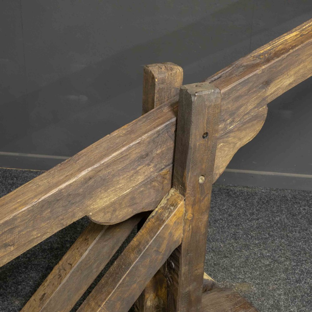 A large dark timber ducking stool featuring a long lever beam, a seated wooden chair at one end, and a heavy support frame on wooden wheels. View IX