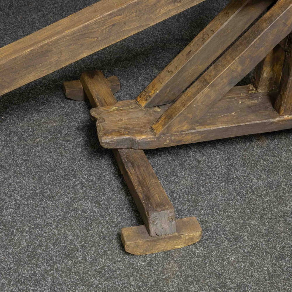 A large dark timber ducking stool featuring a long lever beam, a seated wooden chair at one end, and a heavy support frame on wooden wheels. View X
