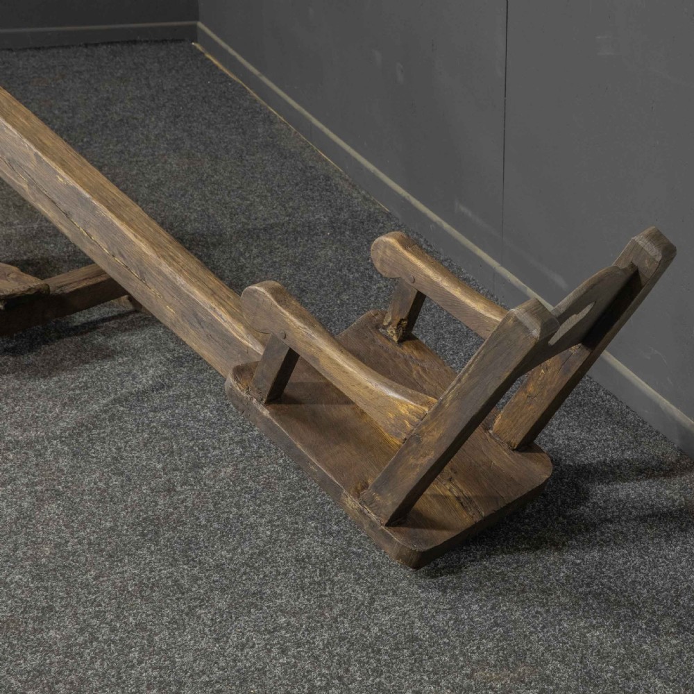 A large dark timber ducking stool featuring a long lever beam, a seated wooden chair at one end, and a heavy support frame on wooden wheels. View XXIII