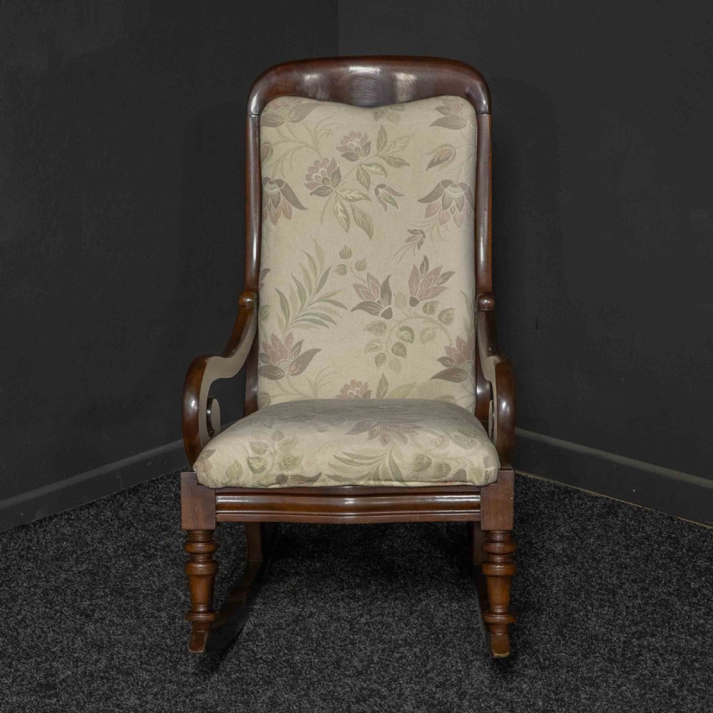 A Victorian rocking chair crafted from dark polished mahogany with scroll arms, turned front legs, and cream floral upholstery. View II