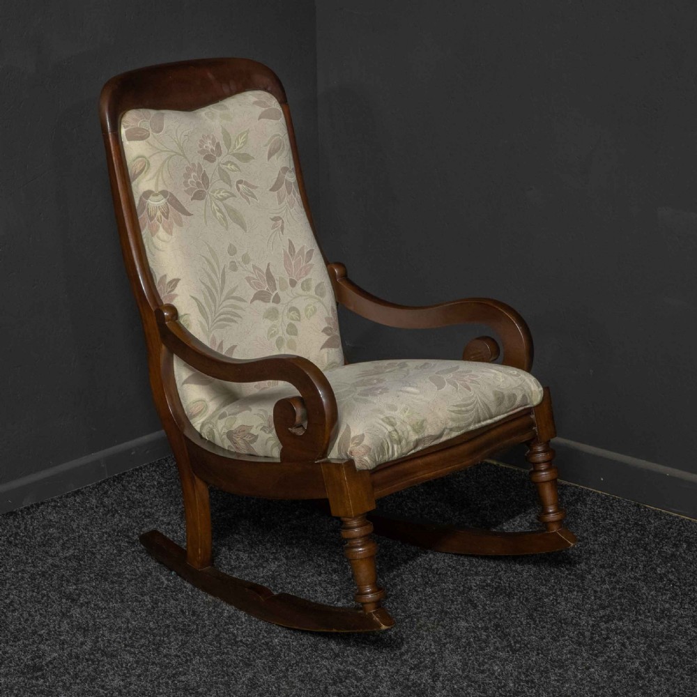 A Victorian rocking chair crafted from dark polished mahogany with scroll arms, turned front legs, and cream floral upholstery. View III