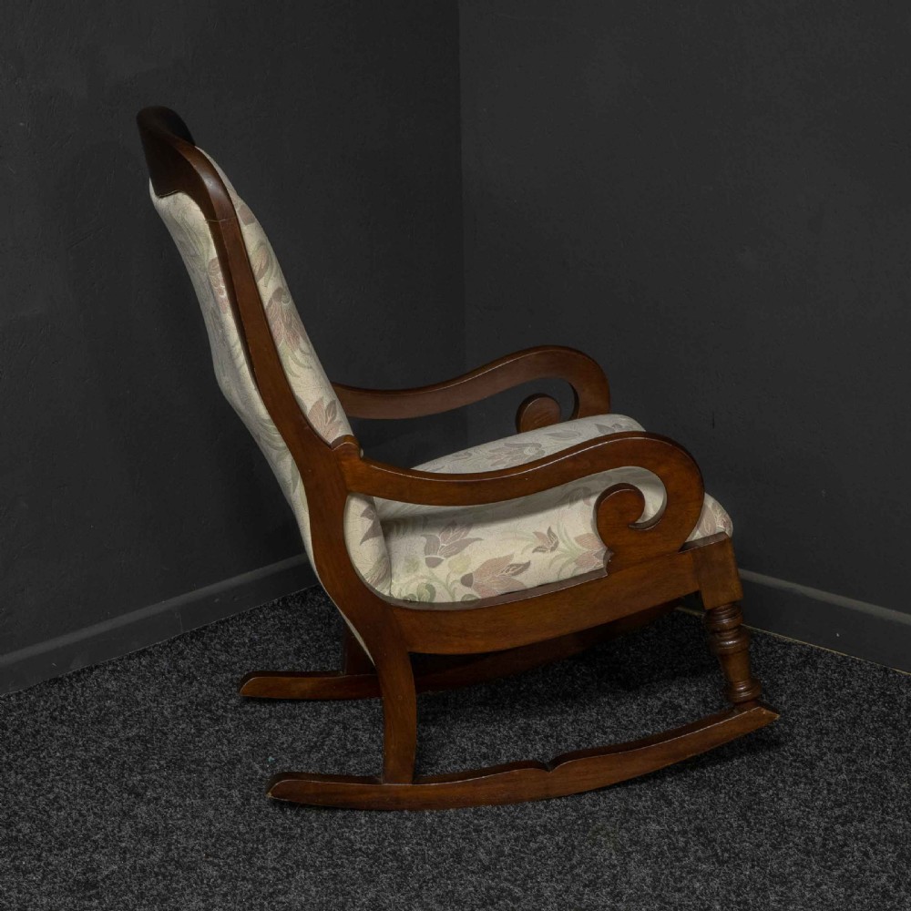 A Victorian rocking chair crafted from dark polished mahogany with scroll arms, turned front legs, and cream floral upholstery. View IV
