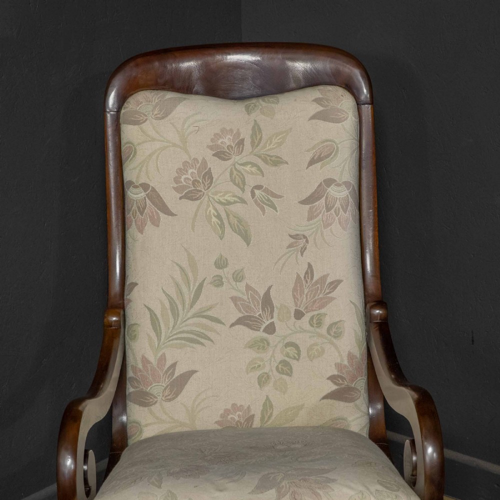 A Victorian rocking chair crafted from dark polished mahogany with scroll arms, turned front legs, and cream floral upholstery. View V