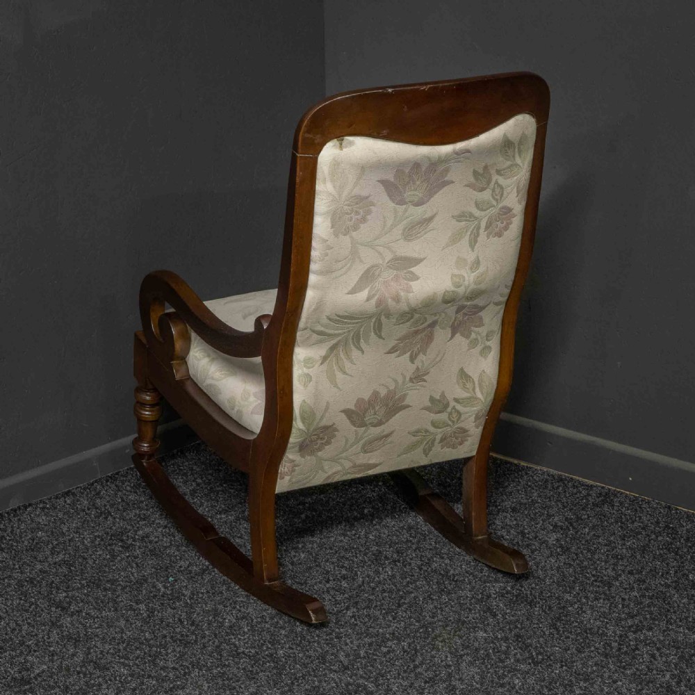 A Victorian rocking chair crafted from dark polished mahogany with scroll arms, turned front legs, and cream floral upholstery. View VII