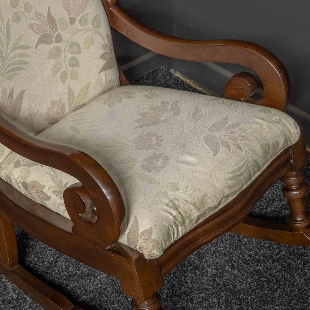 A Victorian rocking chair crafted from dark polished mahogany with scroll arms, turned front legs, and cream floral upholstery. View VIII