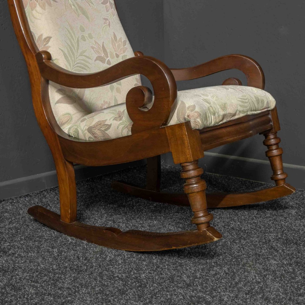 A Victorian rocking chair crafted from dark polished mahogany with scroll arms, turned front legs, and cream floral upholstery. View IX