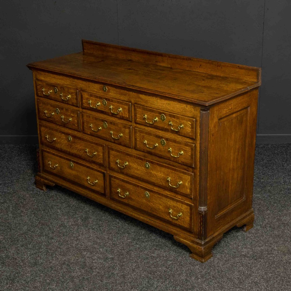 An 18th-century Georgian oak Lancashire mule chest with crossbanded drawer fronts, brass swan-neck handles, and bracket feet. View XI